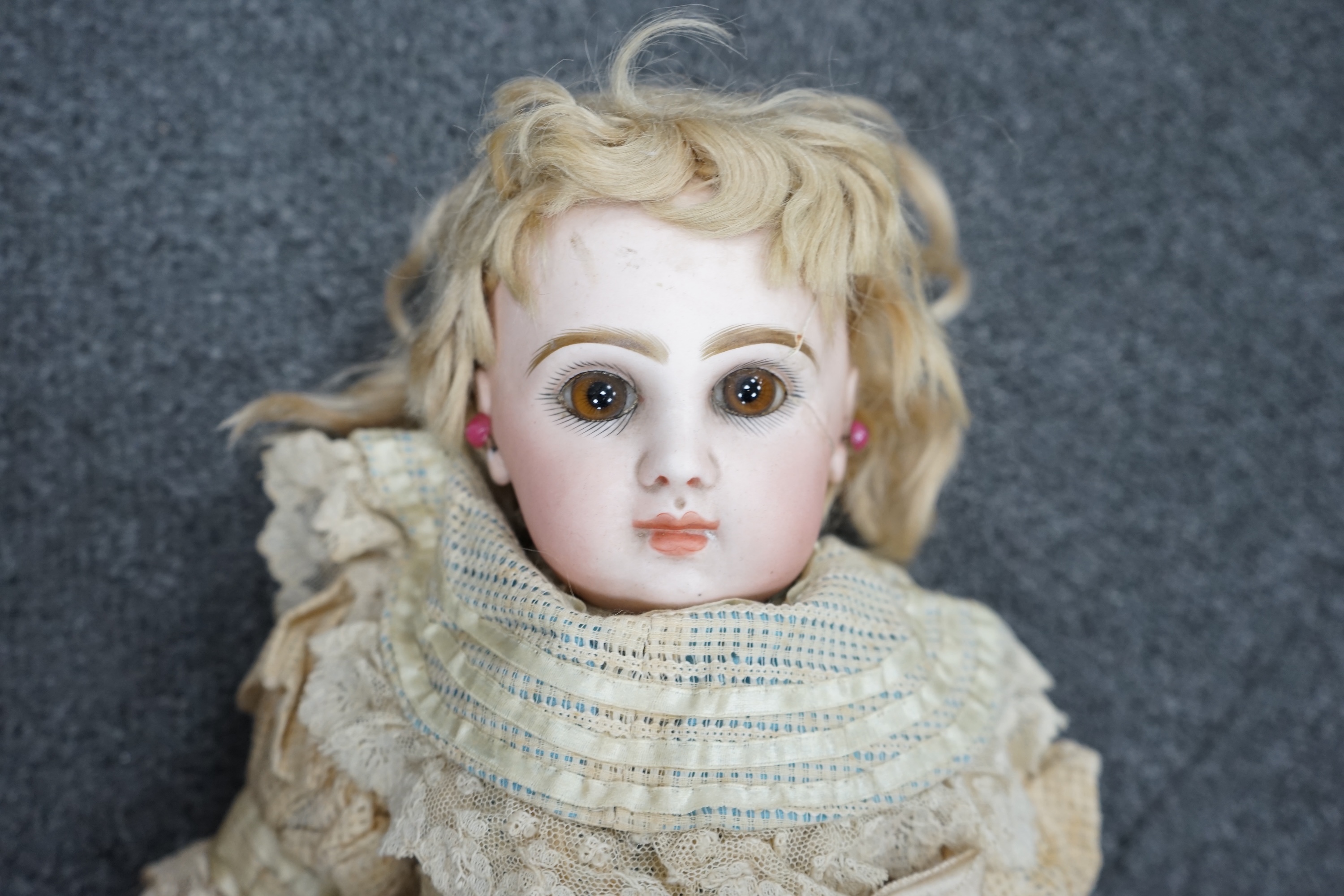 A Tête Jumeau bisque doll, closed mouth and paperweight eyes, jointed wood and composition body, two other French bisque dolls and assorted clothing, all contained within a three-layer wood and metal-bound cabin trunk, J